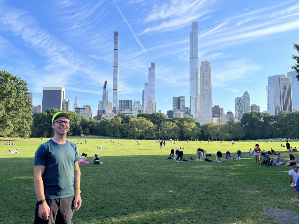 Man standing in Sheep Meadow with skyline of 60th St Manhattan in background