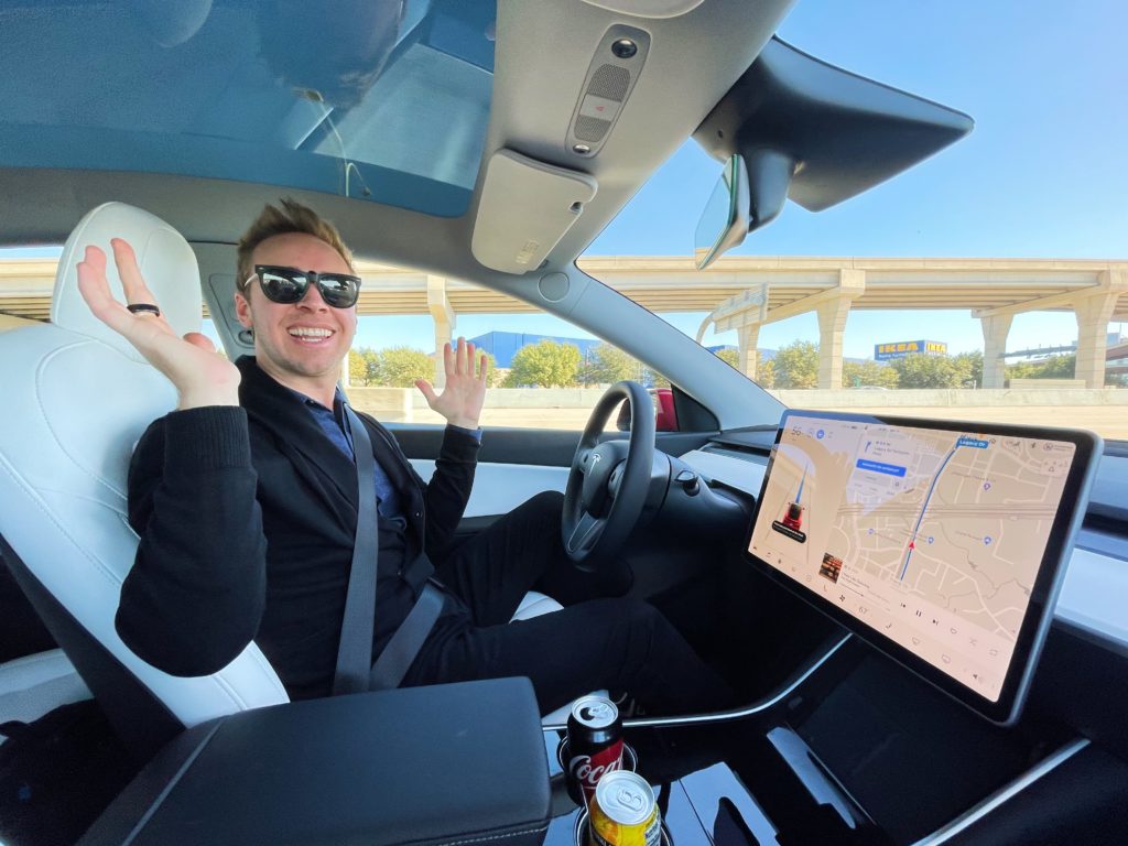 man sitting in driver's seat of Tesla Model Y car, looking at camera and smiling (Nick Gray)