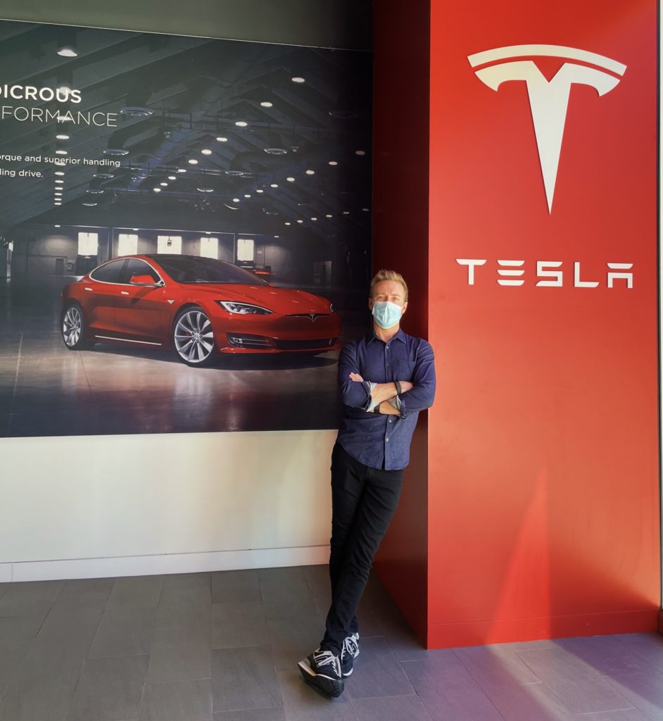 man standing inside Tesla sales office in Texas, red Tesla banner and logo behind