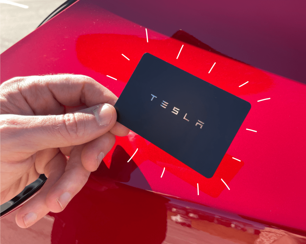Hand holding a black Tesla key card, with a red background color