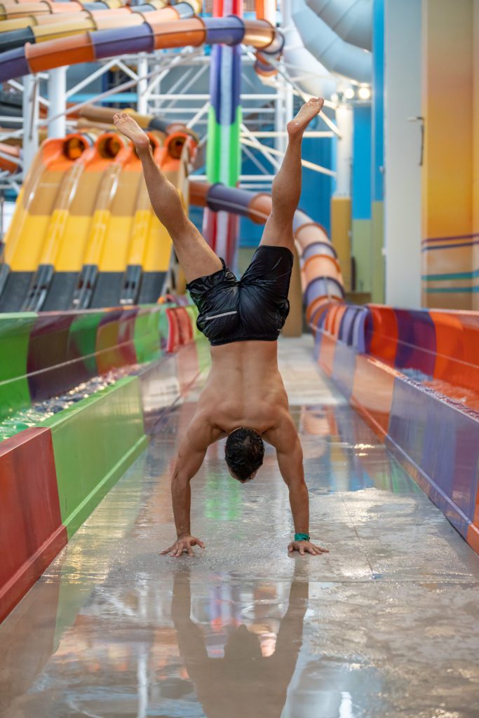 brown man doing a handstand at an indoor water park