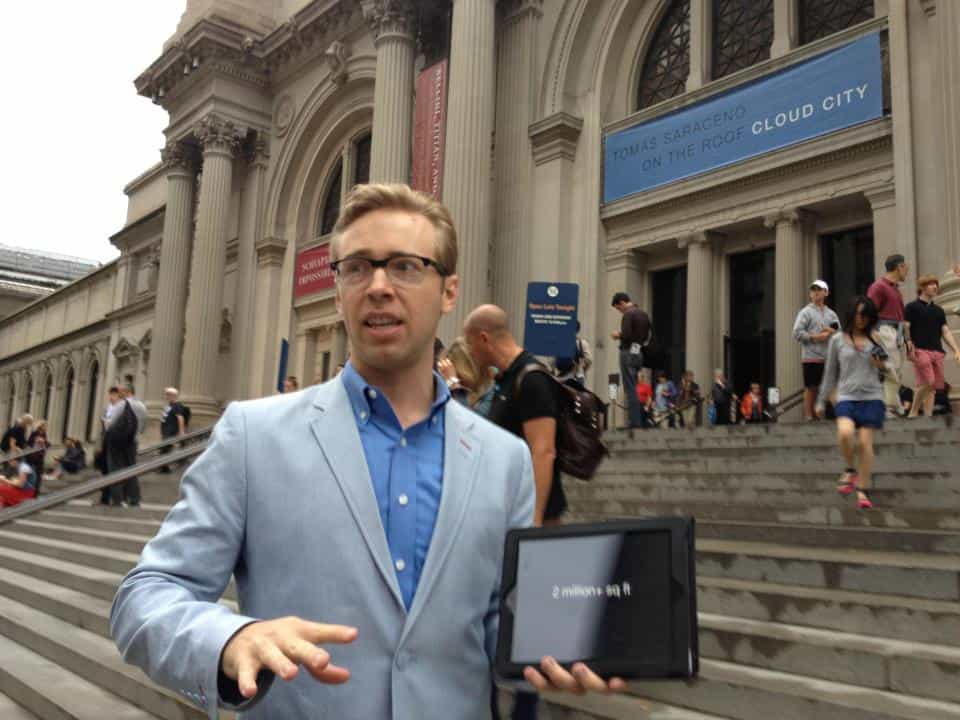 Man wearing blue blazer and holding iPad standing outside of the Metropolitan Museum of Art