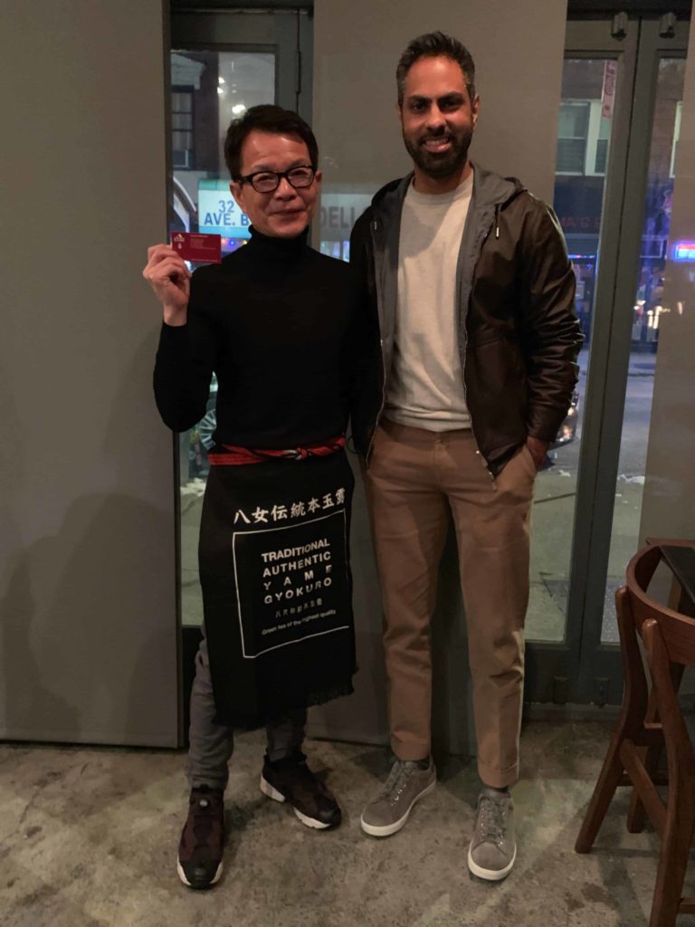 Picture of Takao Shiimado wearing all black and holding his business card. Ramit Sethi is standing to his right.