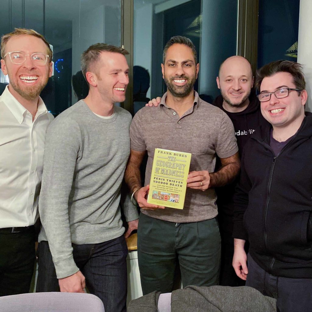 Five men standing close together holding the book in the middle
