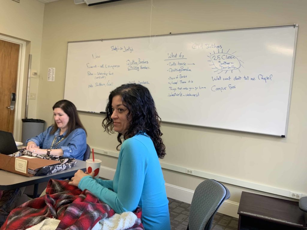Two women in a classroom with ideas on the whiteboard behind them