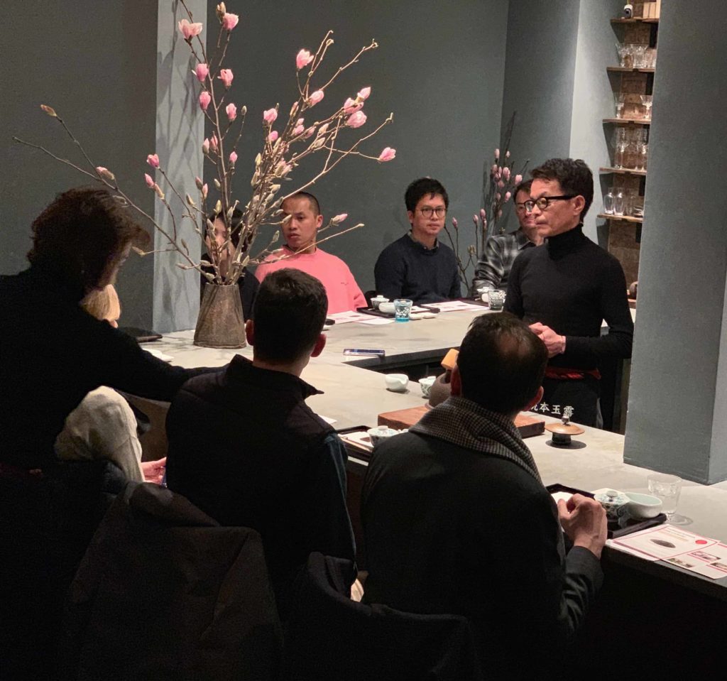 Man at a counter, and people sitting around the counter, indoors at a tea house 29B teahouse in Manhattan NYC