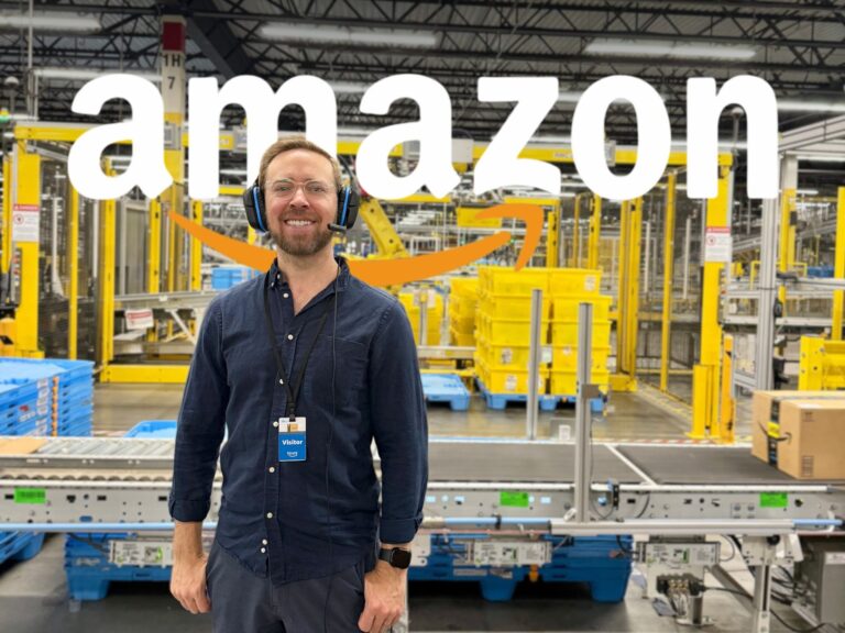 Nick Gray standing inside of an Amazon warehouse with the Amazon logo behind him.