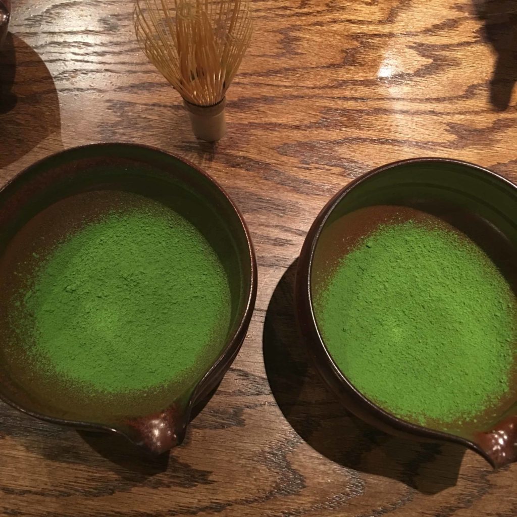 Two bowls of matcha powder, with matcha whisk on top