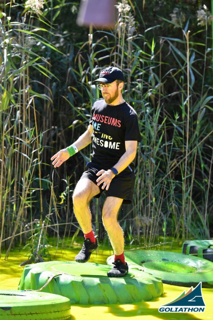 Man jumping across tires in green water at an obstacle course race