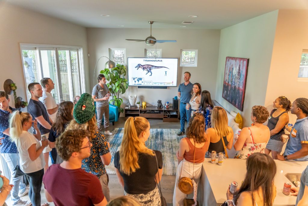 people gathering around a large screen with a T-Rex to learn dinosaur facts at a dinosaur party
