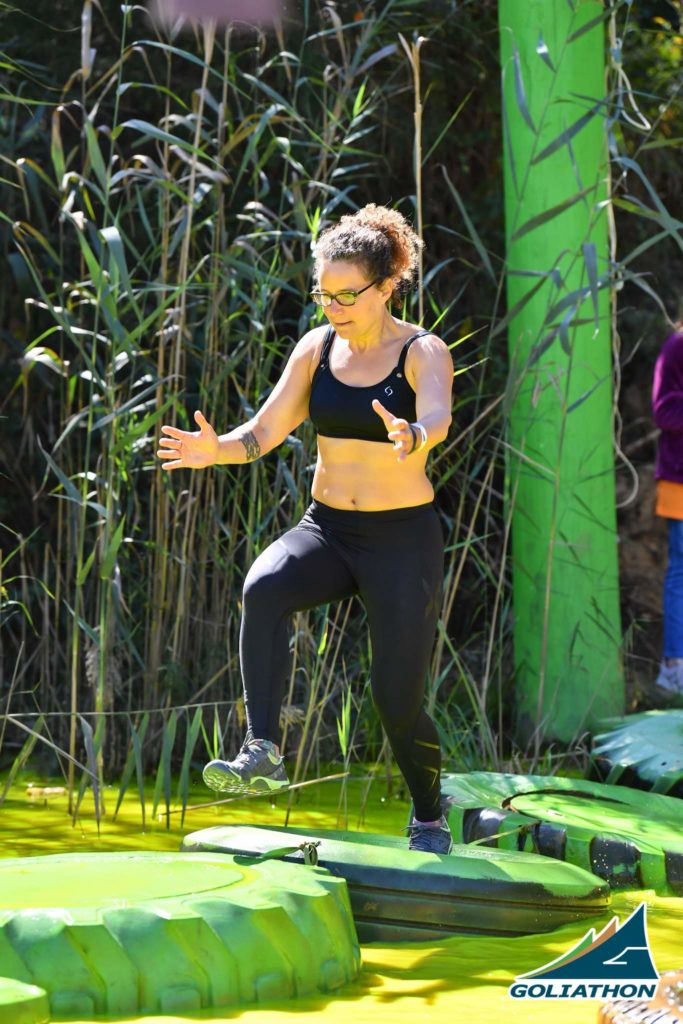 Woman running across tires in water at an obstacle course