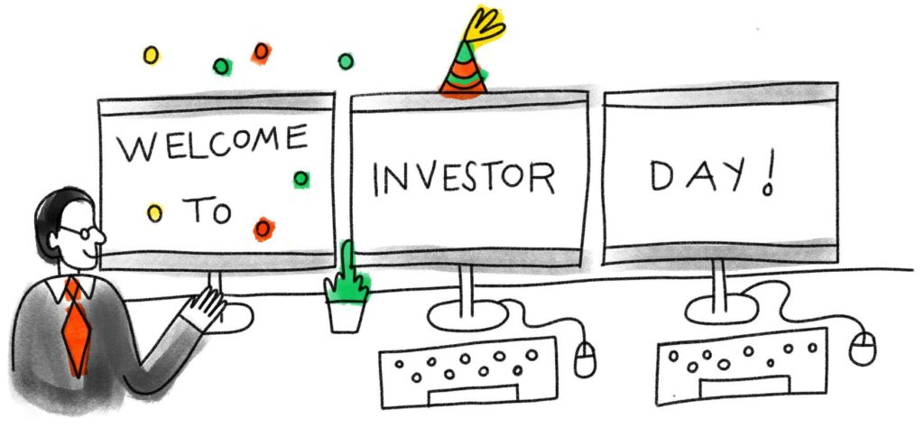 Person in front of three computer screens, they say: WELCOME TO INVESTOR DAY