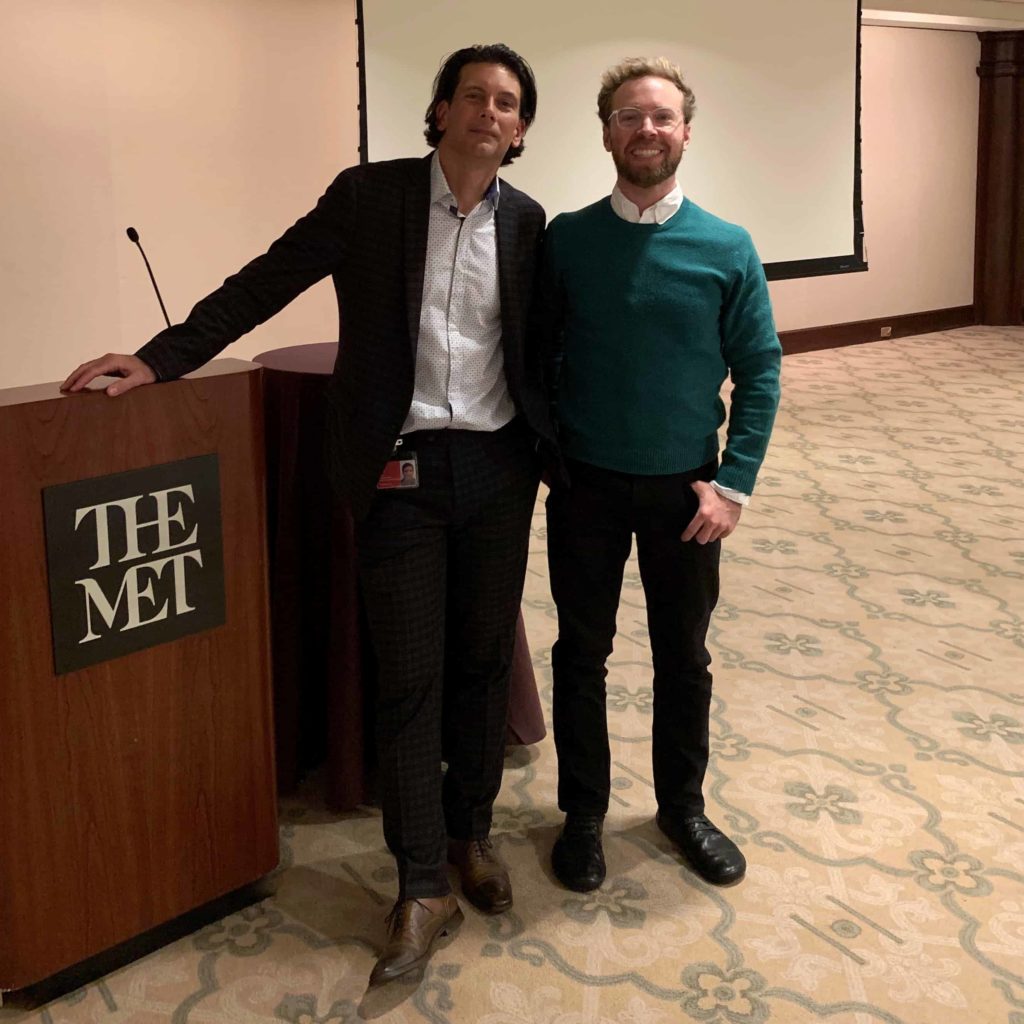 Two men standing near a wooden podium with The Met logo