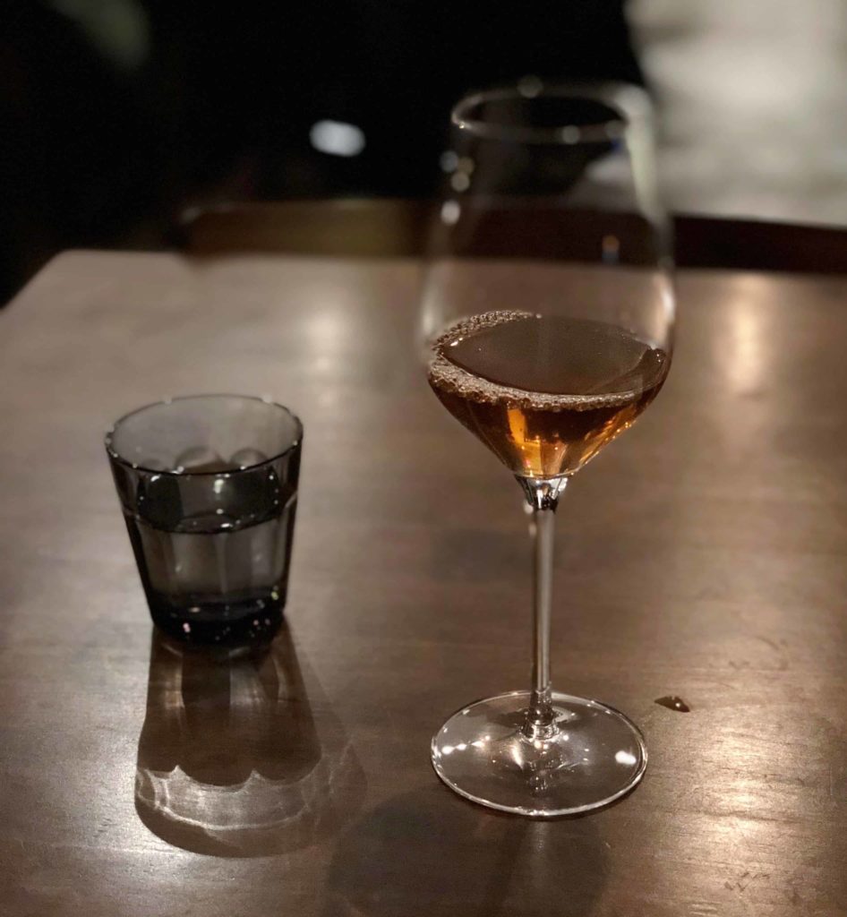 Table with two glasses: water cup on left, and wine glass with hojicha tea on right