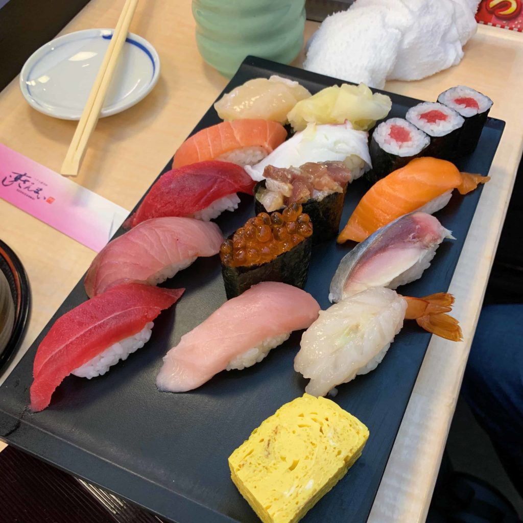 Black plate with about 15 pieces of nigiri sushi of various pretty colors
