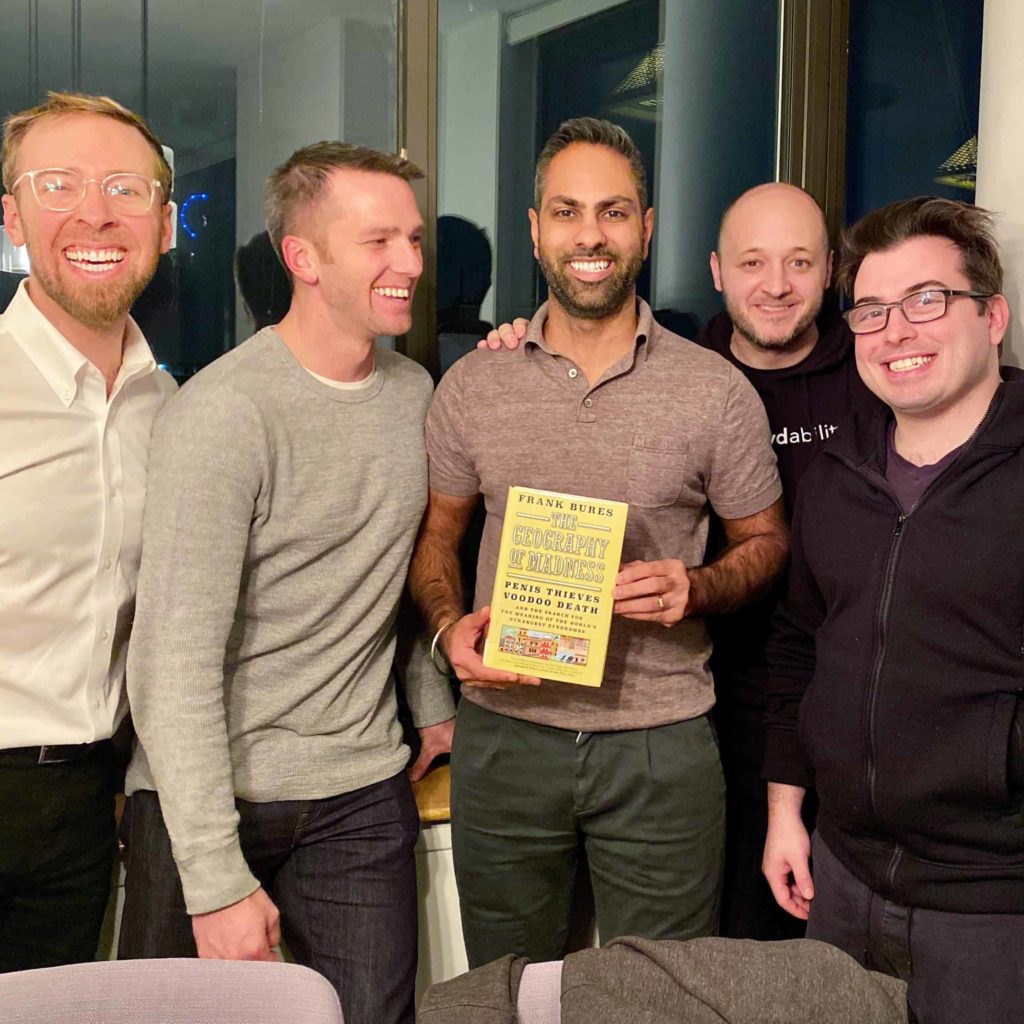 Five men standing close together holding the book in the middle