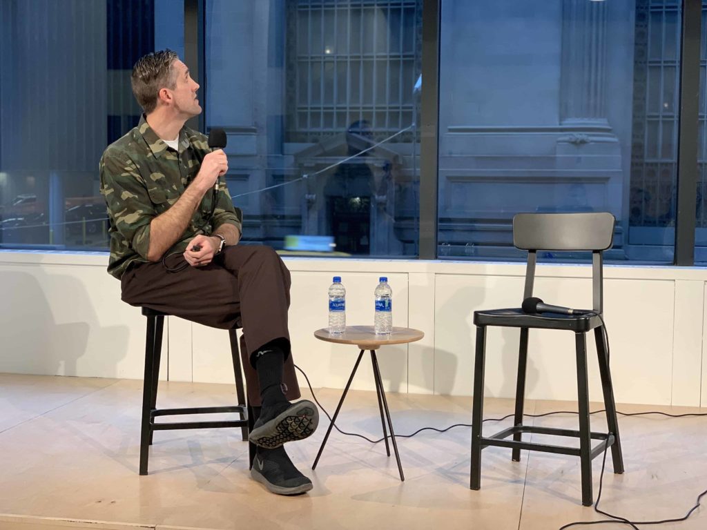 Man on stage wearing camo sitting in a chair