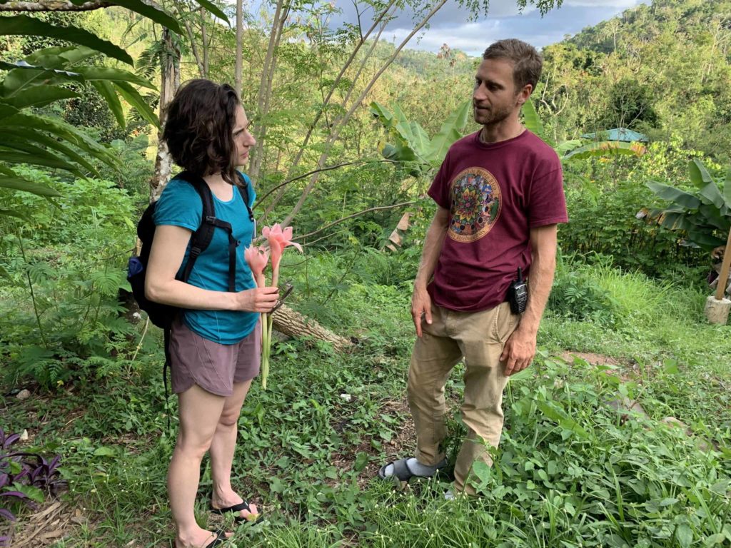 Woman holding two flowers, Owen a founder of Plenitud wearing a maroon shirt