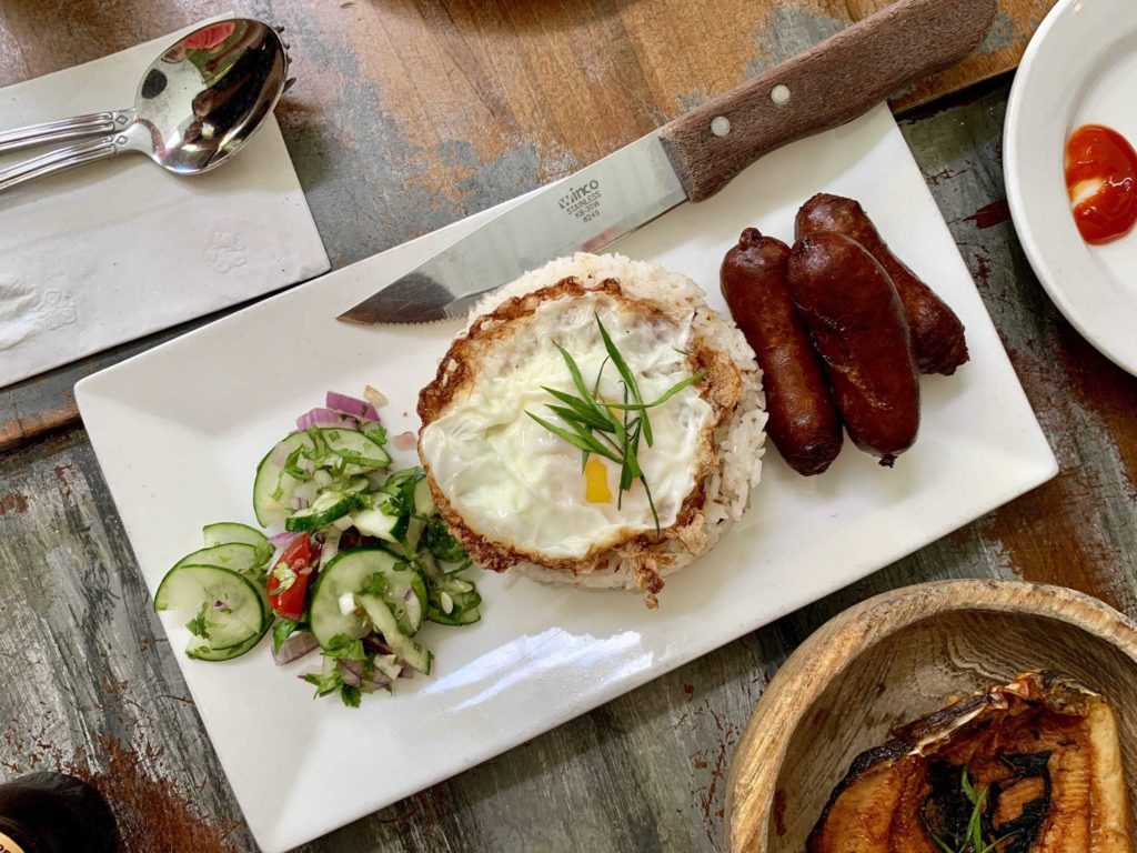 Plate has cucumbers, egg / rice, and sausages on it. Looking overhead at the table