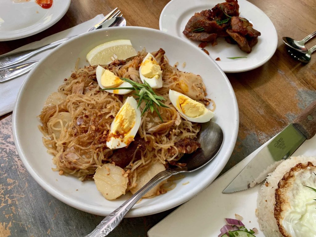 White plate has noodles with sliced eggs on top, smaller plate in back with fried pork