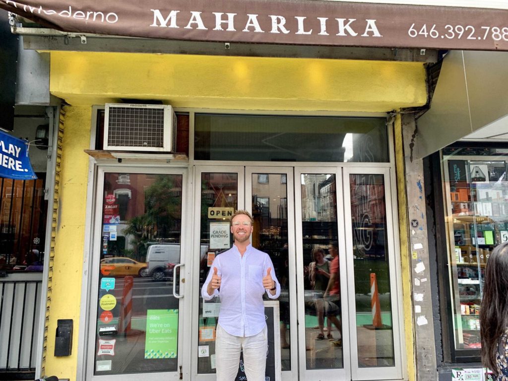 White guy (me) wearing long-sleeve white shirt and white pants standing in front of a restaurant facade on street of NYC