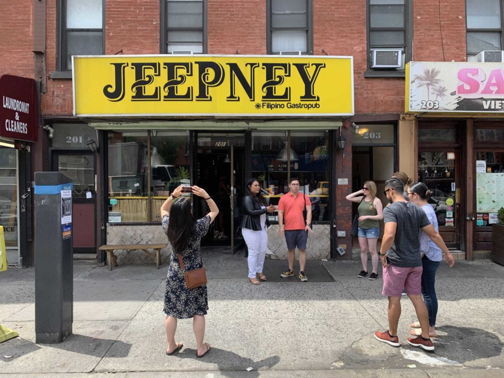 Jeepney yellow storefront and sign of restaurant in New York City, with people taking pictures and standing underneath the awning