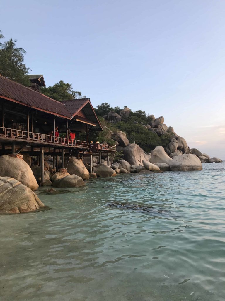 Large rocks, and a restaurant on the shoreline. Nice color water