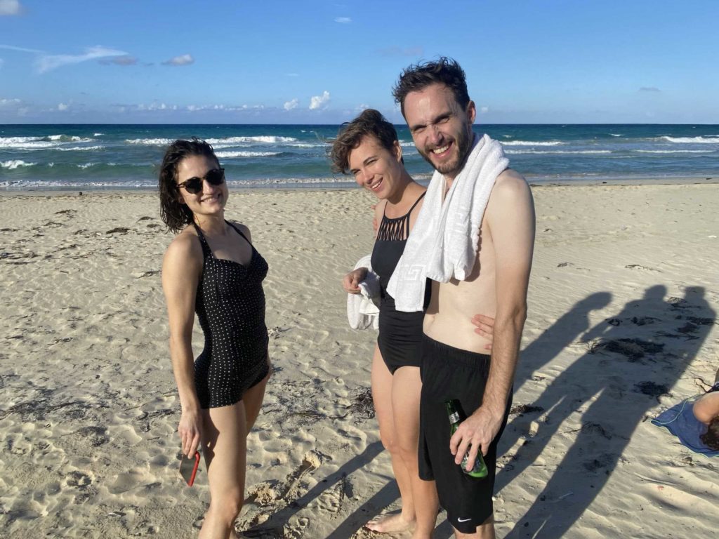 Three white people at the beach, with sand and ocean in the background