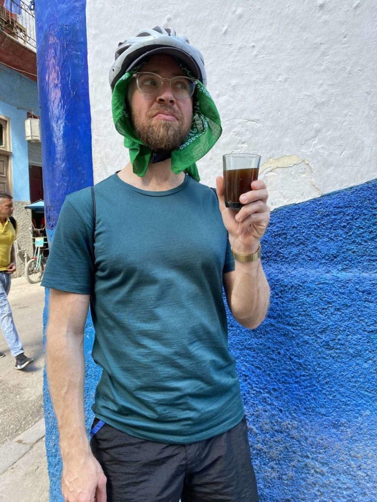 White man holding a cup of black coffee wearing helmet with green bandana