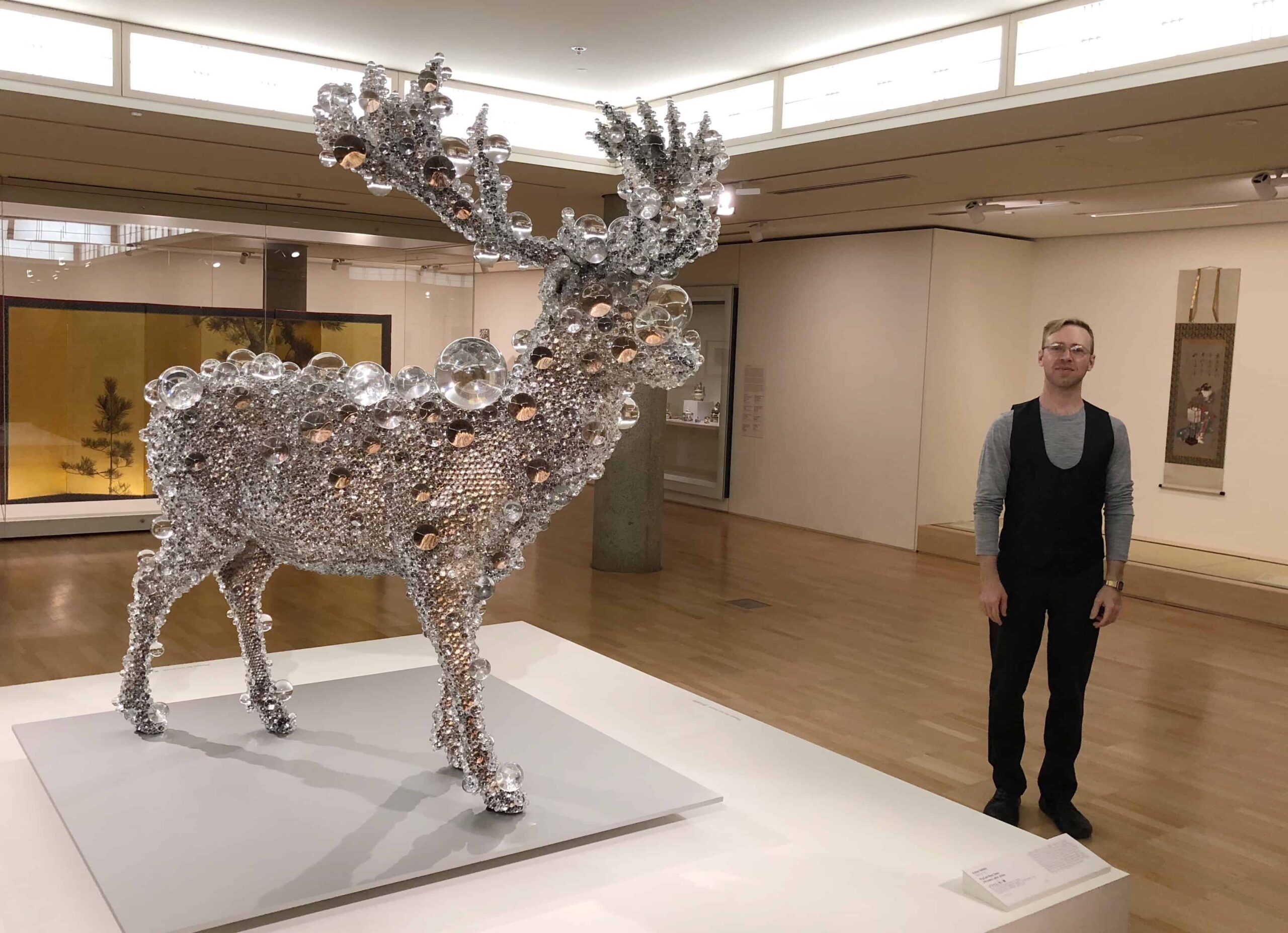 Deer with many glass beads, plus awkward American gentleman standing to the right of it in a vest and black slacks