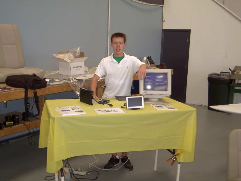 Yellow table and electronic equipment on top, me standing behind it with my arm on a computer