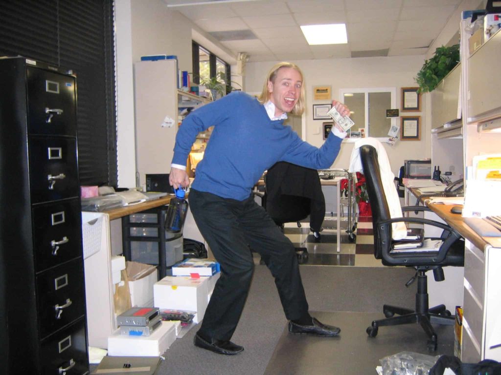 Man in a blue sweater in an office making a funny post