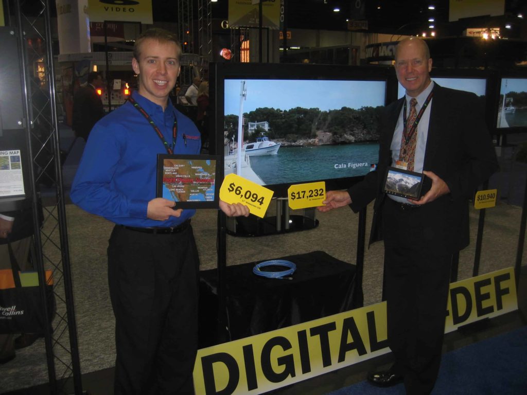 Two people holding yellow signs in front of an LCD monitor
