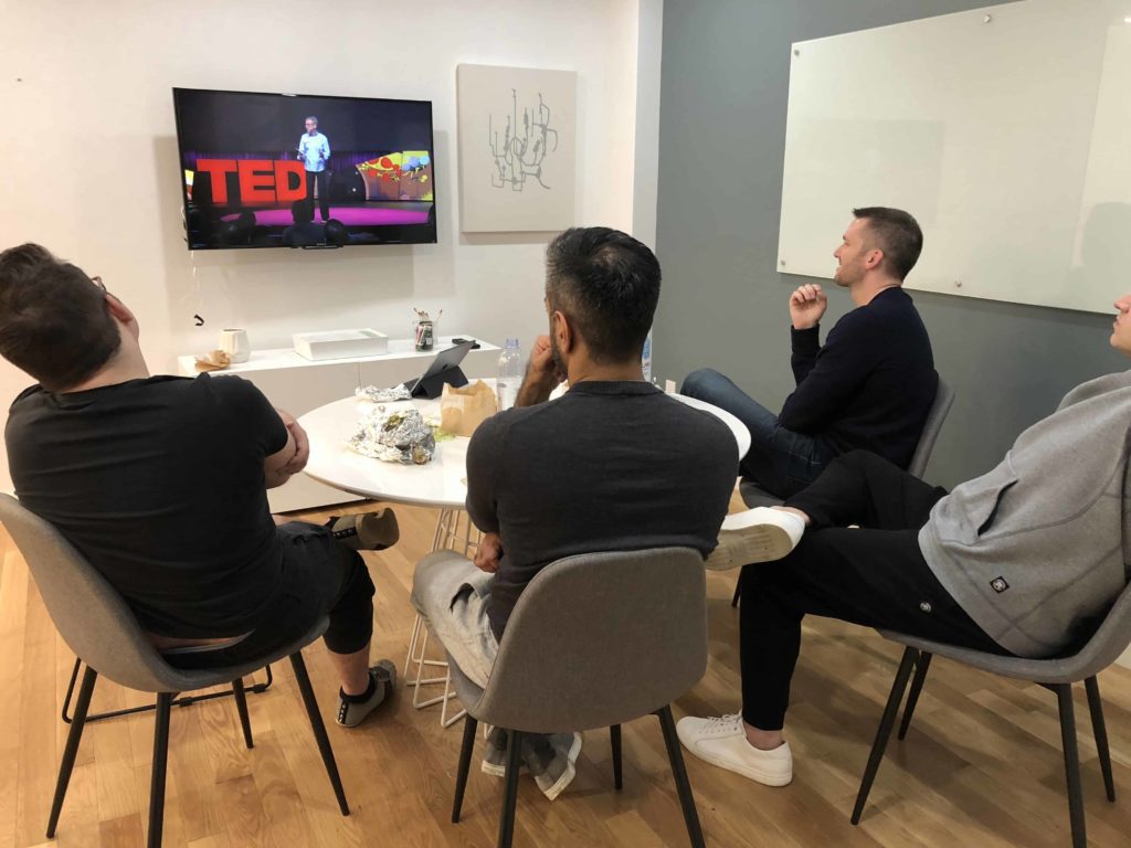 Four men watching a TED Talk by John Doerr in a conference room