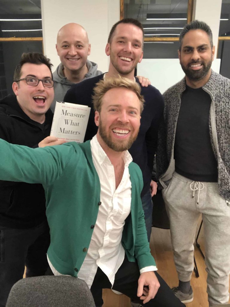 Attractive gentlemen plus one guy holding a copy of the book Measure What Matters by John Doerr
