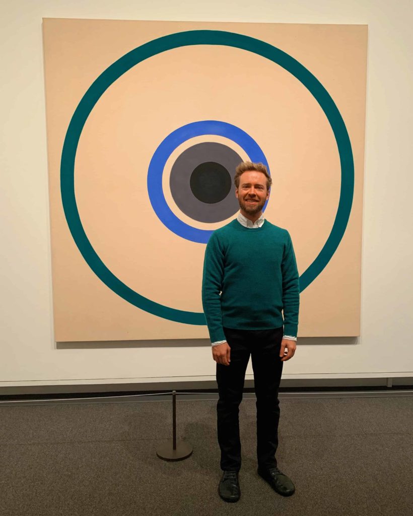 Man in front of a painting that just has circles on it on a white canvas