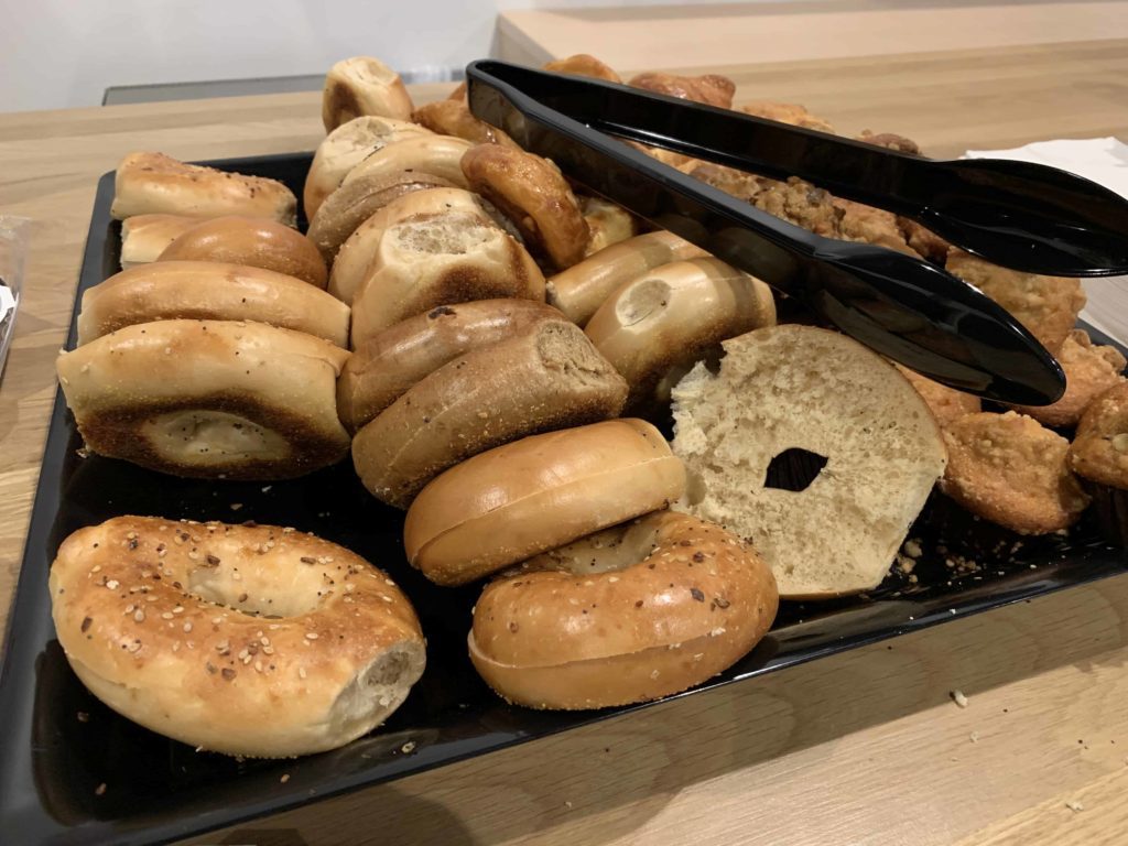 Approx two dozen bagels on display with tongs