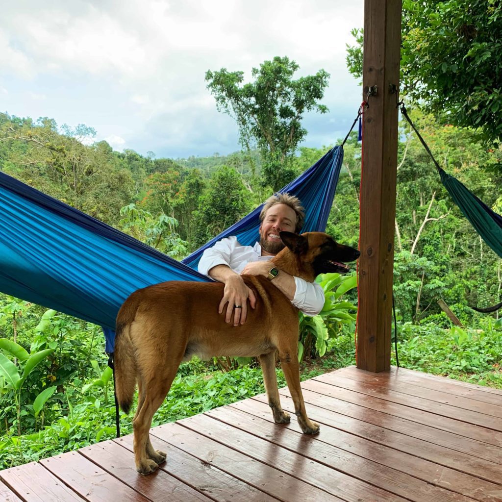 Man hugging a dog while he lays in a hammock