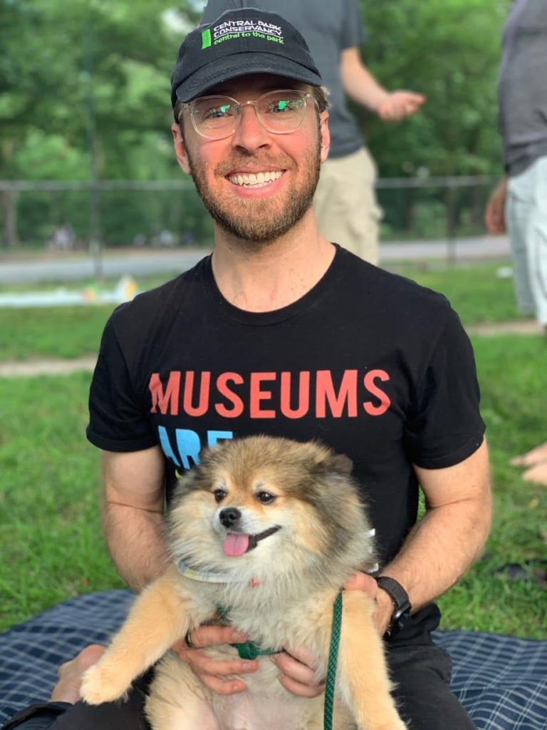 White man wearing glasses and a Central Park hat holding a small dog (the man is me)