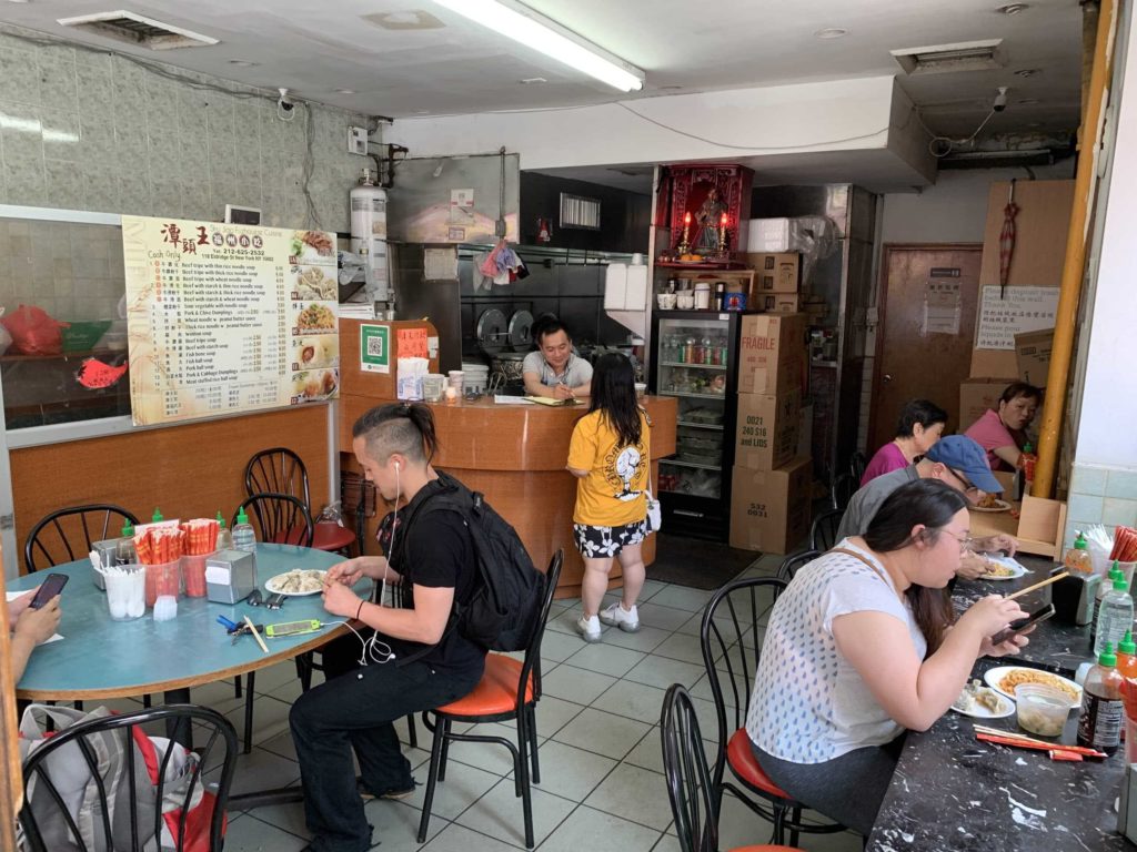Interior of a Chinese restaurant: people sitting at chairs, eating food, and a cashier in the back
