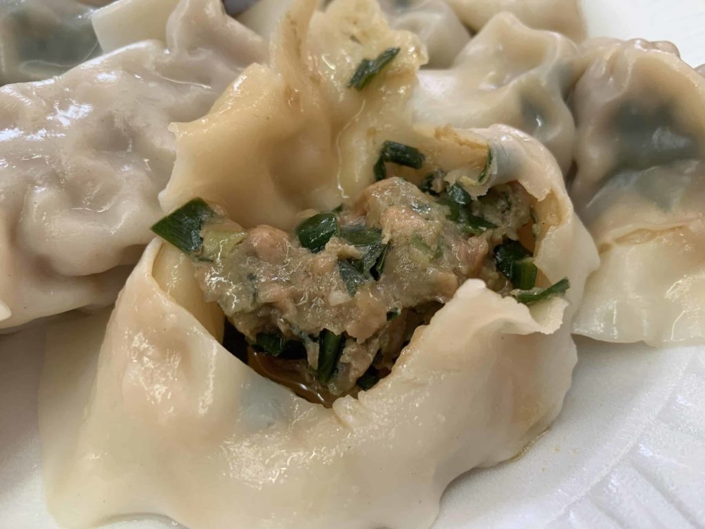 Close-up view of a torn dumpling showing the interior sausage-like view of pork and chive