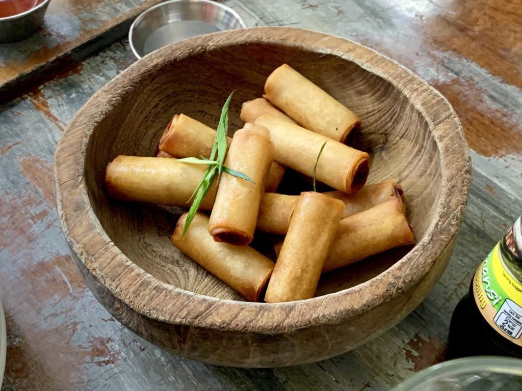 Wooden bowl with 8 or so spring rolls inside, golden brown in color