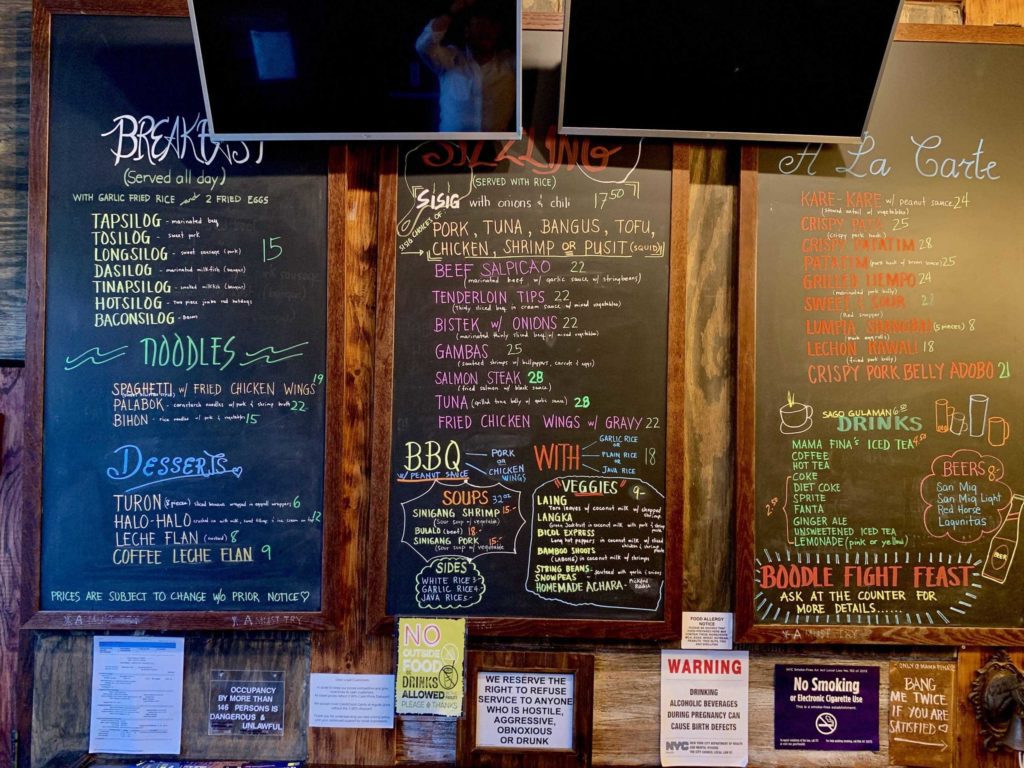 Three-panel menu on the wall which lists many restaurant items written on black boards in colored marker or chalk