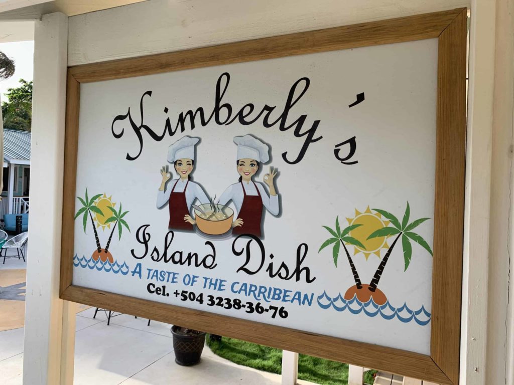 Sign for Kimberly’s Island Dish in Roatan, with a colorful drawn image of two chefs and some palm trees