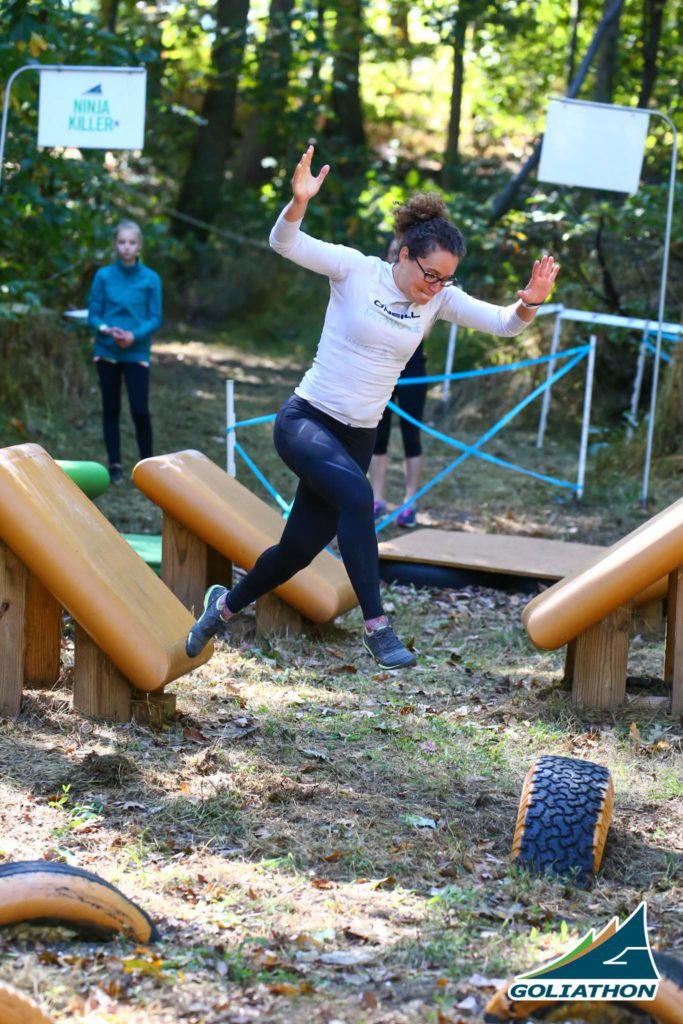 Woman jumping between a board and a tire at an obstacle race
