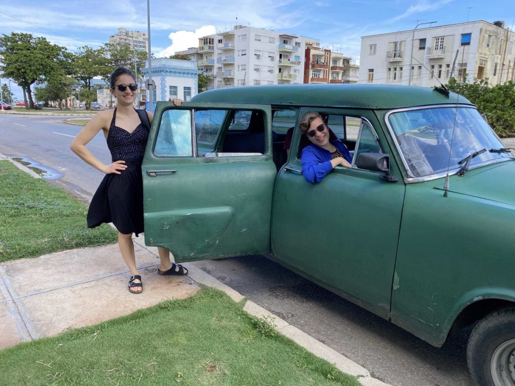 Two women smiling with a very old green car