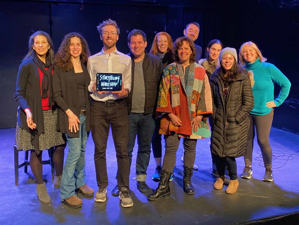 Group of people on stage, with me (center) holding a sign that says Storytelling Workshop