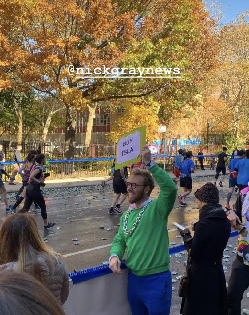 Nick Gray (that's me) holding a sign that says BUY TSLA at the New York City Marathon in 2018, standing on side of road while runners run in the background