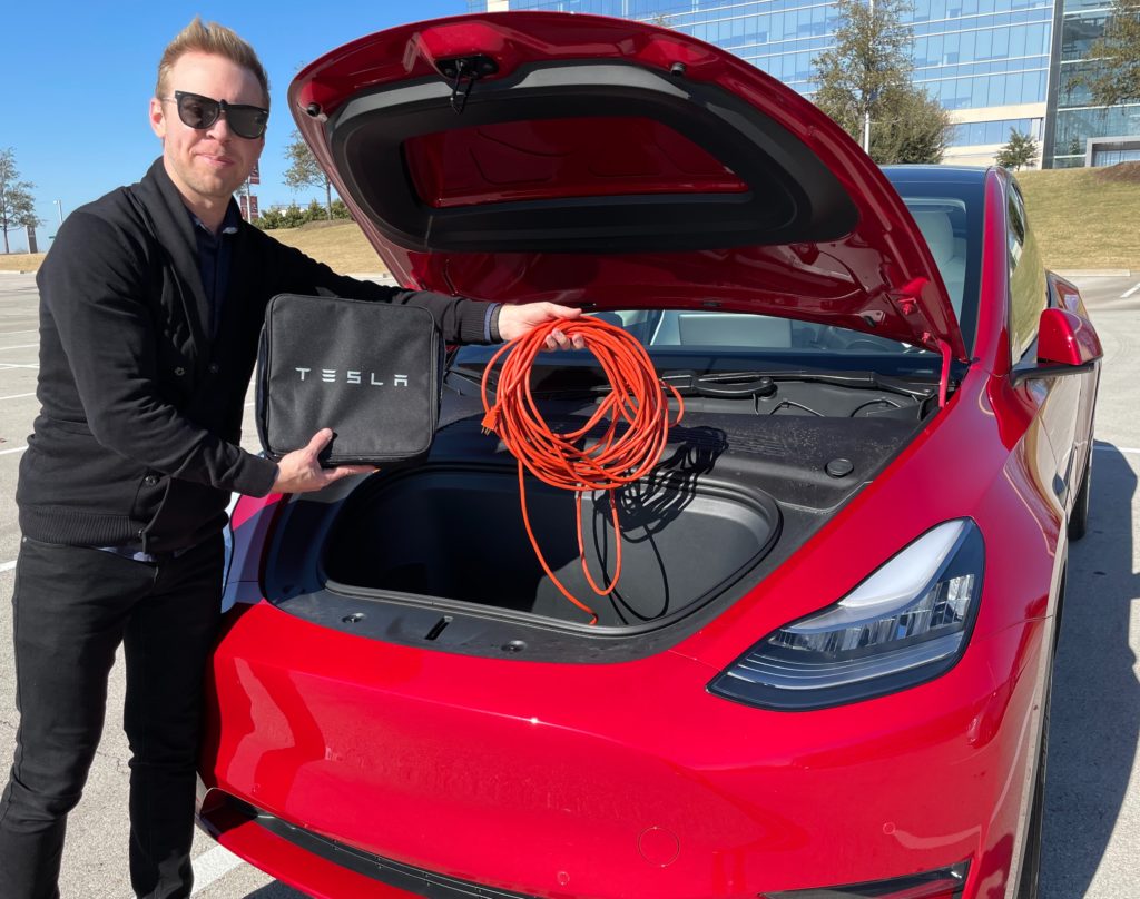 man standing in front of a Tesla Model Y with the front trunk open (frunk) holding electric extension cord