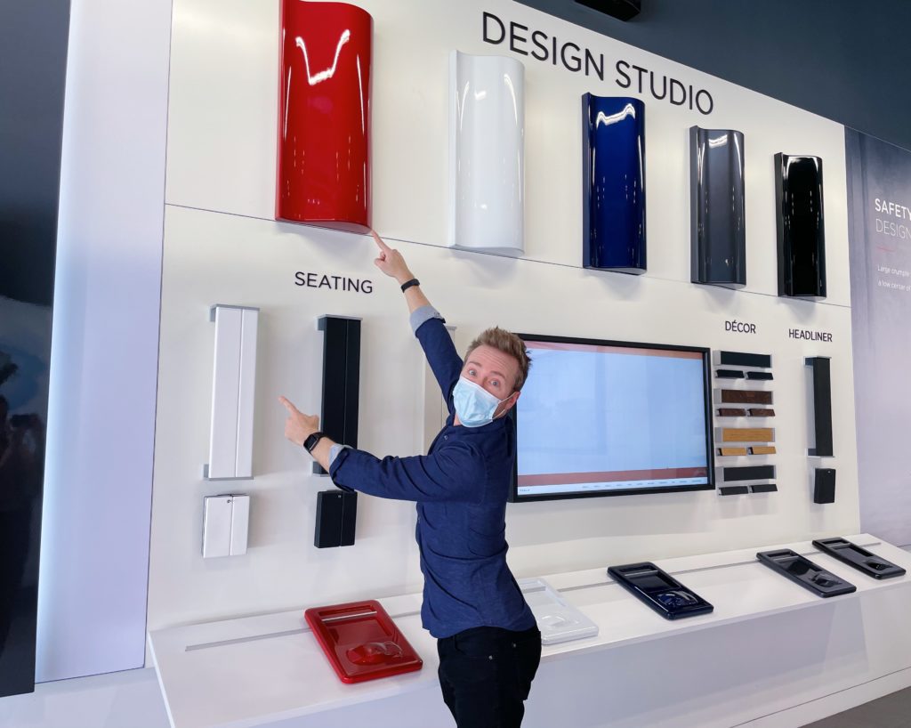 man pointing at wall which says DESIGN STUDIO up top, pointing to red panel and white SEATING panel colors